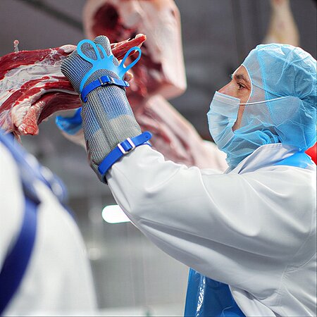 Mitarbeiterin in Hygienekleidung bearbeitet Schweinefleisch an einer Verarbeitungslinie bei WestCrown.