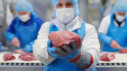 Mitarbeitende in Hygienekleidung präsentieren und bearbeiten Schweinefleischstücke an einer Verarbeitungslinie bei WestCrown.