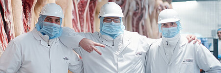 Drei WestCrown-Mitarbeitende in Hygienekleidung stehen gemeinsam vor Schweinehälften im Produktionsbereich.