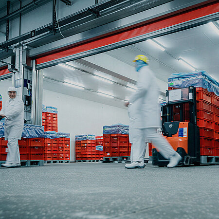 Mitarbeitende in Hygienekleidung bewegen rote Transportkisten in einem Produktions- und Logistikbereich von WestCrown.