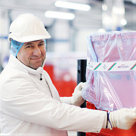 Mitarbeiter von WestCrown bewegt eine verpackte rote Transportkiste im Produktionsbereich.