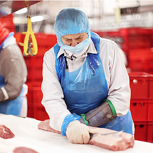 Mitarbeiter in Hygienekleidung zerlegt Schweinefleisch an einem Arbeitstisch im Produktionsbereich von WestCrown.