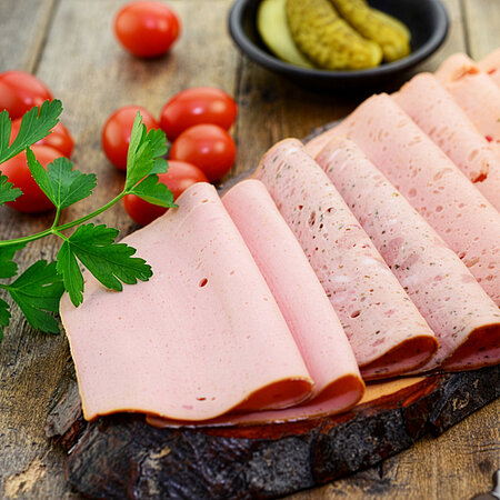 Aufgeschnittene Wurstscheiben auf einem Holzbrett mit Tomaten, Petersilie und Gewürzgurken.