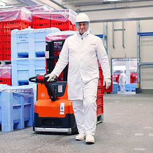 Mitarbeiter in Hygienekleidung bewegt einen elektrischen Hubwagen zwischen Transportkisten im Gefrierhaus von WestCrown.