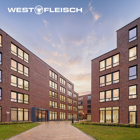 Westfleisch-Verwaltungsgebäude mit beleuchteten Fenstern und Westfleisch-Logo am Abendhimmel.
