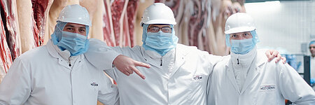 Drei WestCrown-Mitarbeitende in Hygienekleidung stehen gemeinsam vor Schweinehälften im Produktionsbereich.