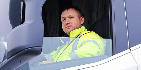 Lkw-Fahrer in Warnschutzjacke sitzt im Fahrerhaus eines WestCrown-Lkw.
