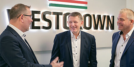 Drei WestCrown-Führungskräfte im Gespräch vor dem beleuchteten WestCrown-Logo.