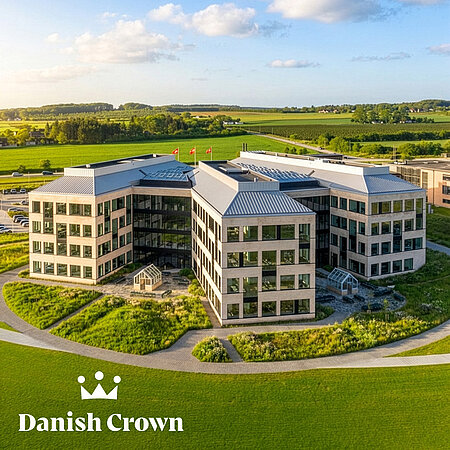 Luftaufnahme eines Danish-Crown-Verwaltungsgebäudes in grüner Landschaft mit Danish-Crown-Logo im Vordergrund.