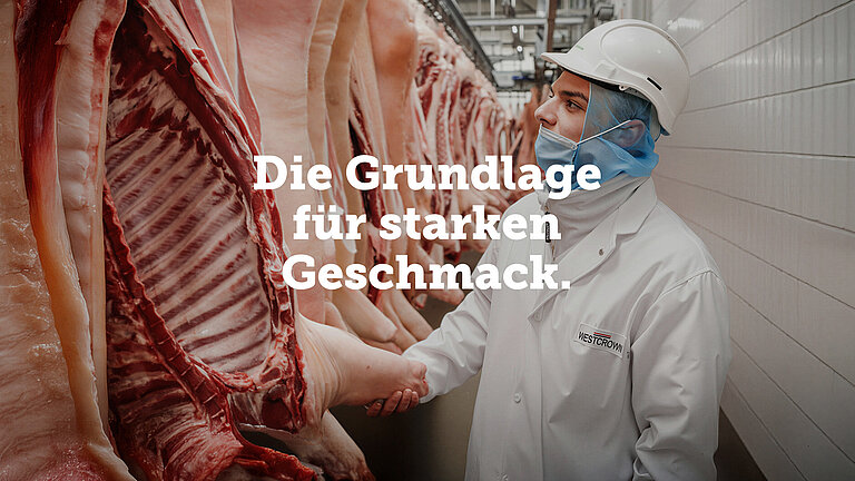 Mitarbeiter von WestCrown kontrolliert Schweinehälften im Produktionsbereich neben dem Schriftzug „Die Grundlage für starken Geschmack.“