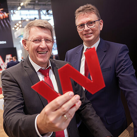 Zwei WestCrown-Vertreter auf einer Messe halten ein rotes W-Logo in die Kamera.