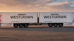 Zwei WestCrown-Sattelzüge mit Markenlogo und Fleischmotiv auf den Aufliegern bei Sonnenuntergang.