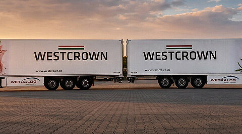 Zwei WestCrown-Sattelzüge mit Markenlogo und Fleischmotiv auf den Aufliegern bei Sonnenuntergang.