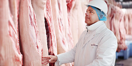 WestCrown-Mitarbeiter in Hygienekleidung prüft Schweinehälften im Produktionsbereich.