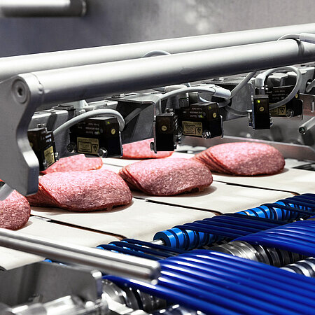 Salami-Produkte laufen auf einem Förderband durch eine automatische Kontroll- und Verarbeitungslinie.